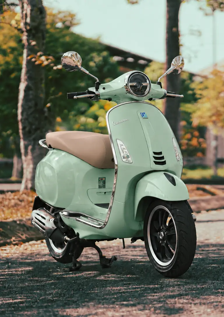 Green Vespa parked on a tree-lined street